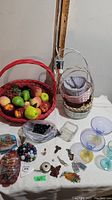 Wide view showing large red basket filled with artificial fruit, smaller woven baskets, glass bowls, assorted marbles, keys, and more.