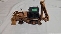 Side angle of the yellow metal Case backhoe tractor toy showing the cab, front loader, and rear digging arm.