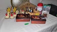 Photo showing entire lot with manger scene, rooster figurines, Norman Rockwell tins, Santa tin, and boxed snowman jar.