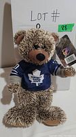 Plush teddy bear facing forward wearing a blue Toronto Maple Leafs jersey with attached tag.