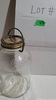 Full view of vintage glass bottle showing metal screw lid and metal handle attached to neck.