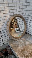 Full view of the round mirror leaning against a textured brick wall showing the entire mirror and frame.