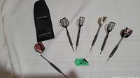 Overview of six steel tip darts with varied flights and a black carrying case.