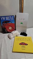 Photo of the Volkswagen Beetle books, white ceramic piggy bank, and black ceramic Avon perfume bottle shaped like a VW Beetle.