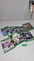 Eight Xbox One game cases arranged on a white surface, showing cover art for NHL hockey games, Madden NFL 18, Splatoon 2, Gears of War 4, and a bowling game.