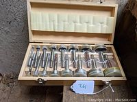 Wooden box containing a complete set of silver metal Forstner drill bits from smallest to largest, placed inside fitted slots with foam padding on the lid.