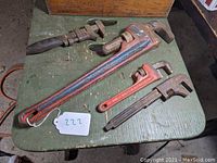 Four wrenches on a green wooden surface showing three pipe wrenches and one old automobile wrench