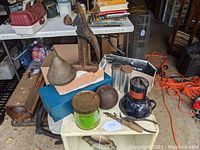 Photo showing an assortment of vintage metal items including a dark cast iron ball, an old Sterno atomizer, metal funnel, steel box, and other small items on a table with various background items.