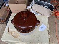 Top and partial side view of the brown glazed pottery bean pot with lid, highlighting the glossy lid and side handles.