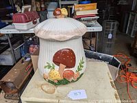 Full view of the white ceramic mushroom cookie jar on a surface with background items.