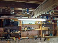 Wide view of wooden shelving filled with various hand tools, C-clamps, containers, and workshop accessories in a basement or workshop environment.