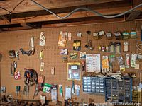 Wide image showing the lighter brown pegboard with various tools, hardware and small items hanging and organized, excluding the darker pegboard with saw blades.