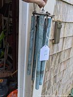 Full view of the copper wind chimes held up, showing all five tubes and hanging ropes.