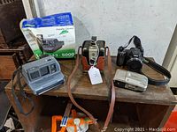 Overview of four vintage cameras including Polaroid Impulse with box, Minolta Vectis 25, vintage Kodak camera in leather case, and compact Kodak camera on wooden surface.
