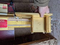 Photo showing the Incra Jig Ultra with a hand holding it, highlighting the gold aluminum frame, ruler markings, and adjustable stops for precision cutting.