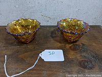 Front view of two amber carnival glass candlestick holders with ruffled edges and floral patterns, placed on wooden surface.