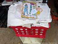 Box containing a pile of sewing patterns, some wrapped in plastic and some loose, with various illustrated covers showing garment images.