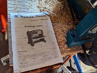 Stapled booklet titled “Makita Planer 304 mm (12”) Model 2012 Instruction Manual” lying on wood shavings