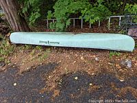 Full side view of the canoe placed upside down on the ground near trees showing the Nature Bound logo and pale green color.