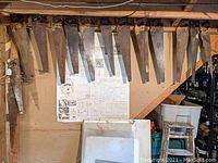 Overall view of vintage wood-handled hand saws hanging on a wall rack, showing varying sizes and conditions