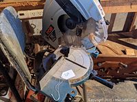 View of the chop saw from above showing the blade, base, and part of the handle, with a tag attached.