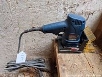 Side view of Ryobi biscuit cutter showing blue body, power cord, and dust cover on workbench.