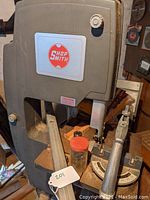 Front view of Shopsmith logo on upper head, shows bandsaw/tablesaw housing and chisel block on table