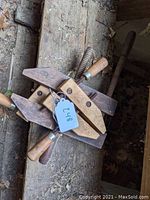 Top view of three wooden woodworking clamps stacked with handles and metal threaded rods visible, tags attached.