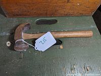 Side view of vintage hammer with curved metal head and wooden handle lying on green surface.