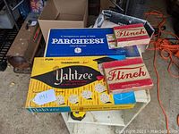 Top view of vintage Parcheesi, Yahtzee, and two Flinch game boxes on table showing original packaging.