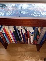 Front view of one wooden side table loaded with reference books on lower shelf