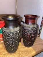 Two carved vases with dark finish and detailed, raised floral and architectural motifs possibly black cinnabar.