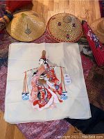 Photo showing two woven straw hats and a square fabric tapestry with Japanese geisha artwork.