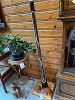 Full view of didgeridoo standing on wooden base next to other furniture