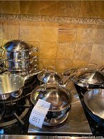Wide view of the cookware collection on a stove including stackable steamer, double boiler, saucepans, skillet, frying pan.