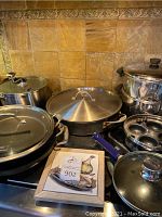 Photo showing multiple covered pans including sauteuse and double boiler set alongside blue handled skillet and egg poacher insert.