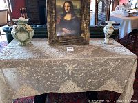 Overview of lot showing table covering, framed Mona Lisa print and two decorative vases