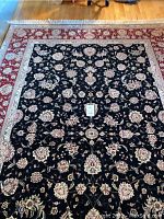 Full view of rug on hardwood floor showing overall floral pattern and red border