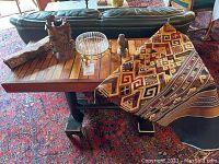 Main shot showing wooden sofa table with slatted top, metal glass dish, carved wooden floral piece, owl figurine and fabric runner draped.