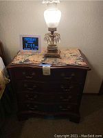 Full front view of the wooden bedside dresser with lamp and digital clock on top.