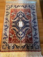 Full view of ornate prayer rug showing entire design and fringe on wood floor.