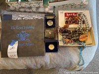 Photo showing The Royal Wedding photograph album, commemorative coins in blue boxes, costume jewelry including pearl and blue bead necklaces, vintage political pins, small music box, and a Dutch Master cigar box.