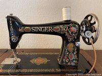 Close-up side view of black enameled Singer machine with gold and red decals showing brand name