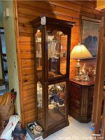 Full front view of cabinet against wood paneled wall showing overall structure, finish and interior shelf arrangement with items inside (items not included).
