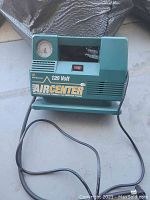 Green Airbender Aircenter 120 Volt battery charger with analog ammeter gauge, power switch, ventilation slits and attached power cord with plug.