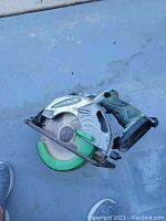 Image of a green and silver Hitachi cordless circular saw model C180MR lying on a blue surface, showing the saw blade and handle.
