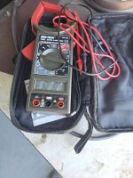 Cen-Tech digital clamp meter with red and black test leads inside a black zippered carrying case on a light surface.
