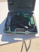 Hitachi FDV 16vB2 corded electric drill in green carrying case with assorted drill bits and black side handle laid inside