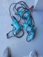 Three Makita electric drills on the floor, connected with power cords