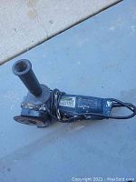 Blue Chicago Electric angle grinder with side handle and power cord coiled around it, showing device and wear details.